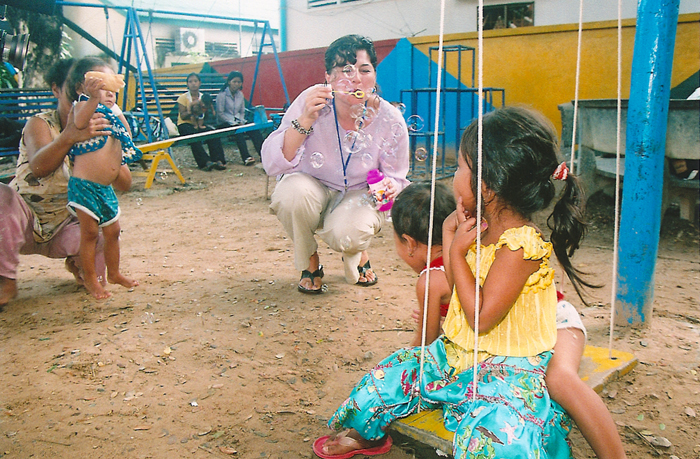 A woman is squatting down to talk to children.
