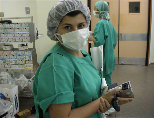 A woman in green scrubs holding a camera.